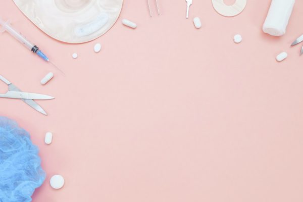 A colostomy bag, pills, medical instruments, a bandage and a medical cap on a pink background.